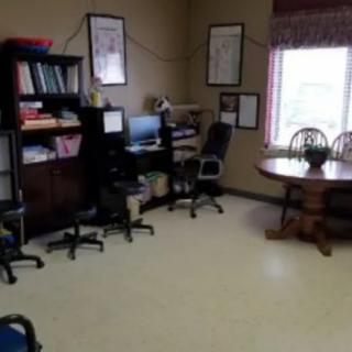 A small office space with a desk, computer, chairs, and a round table by the window.