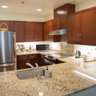 A modern kitchen featuring granite countertops, wood cabinets, and stainless steel appliances.