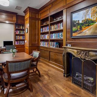 A cozy library room featuring wooden bookshelves, a fireplace, and a meeting table.