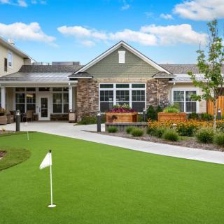 A residential building with a landscaped yard and a small putting green under a clear blue sky.