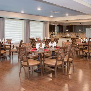 A spacious dining room with elegantly set tables and a modern kitchen in the background.