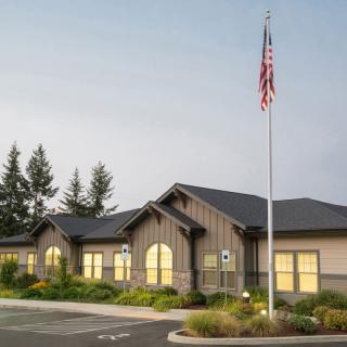 A single-story building with an American flag flying in front, surrounded by trees and landscaping.