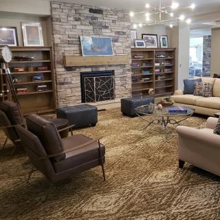 A cozy living room with a stone fireplace, bookshelves, and comfortable seating arranged around a central area rug.