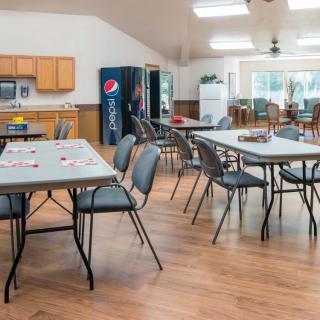 A spacious community center room with tables and chairs, a vending machine, and a small kitchen area.