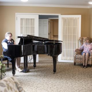 A person playing the piano in a cozy living room setting while another person sits and relaxes.