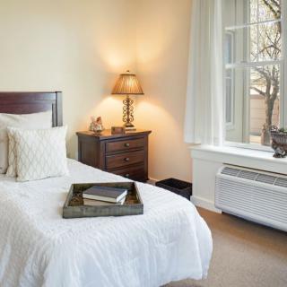 A cozy bedroom with a neatly made bed, bedside lamp, and window.