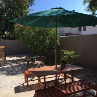 A sunny backyard patio with outdoor furniture and a green umbrella.