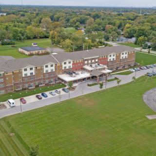 Aerial view of a hotel surrounded by lush greenery and a spacious parking lot.