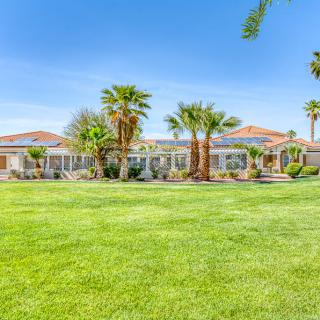 A view of a large house surrounded by palm trees and a well-maintained lawn under a clear blue sky.