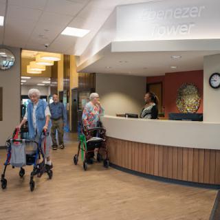 Elderly individuals entering a healthcare facility, assisted by walking aids, with staff at the reception.