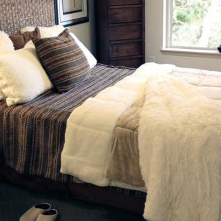 A cozy bedroom setting with a bed covered in a striped blanket and multiple pillows, next to a large window.