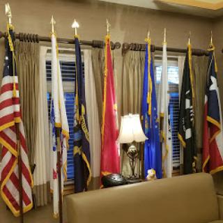 A display of various flags representing military branches and the United States in a decorated interior space.