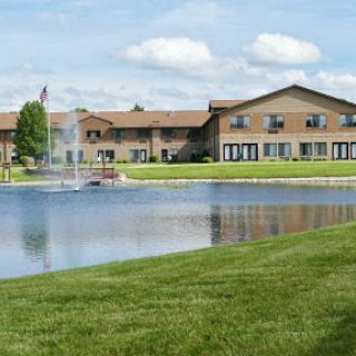 A scenic view of a residential building next to a serene pond under a clear blue sky.