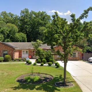 A suburban house with a well-maintained lawn and landscaping, featuring a brick exterior and a driveway.
