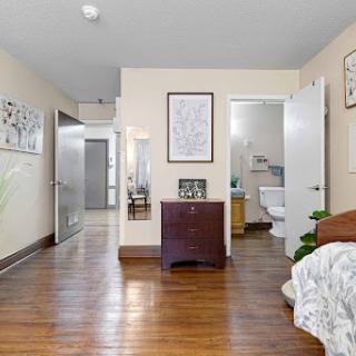 A cozy bedroom featuring wooden flooring, decorative wall art, and an adjacent bathroom.