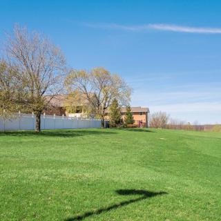 A sunny landscape featuring a house surrounded by trees and a fence, with green grass in the foreground.