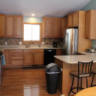 A modern kitchen with wooden cabinets, stainless steel appliances, and a central island with a bar stool.