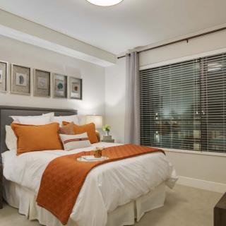 A cozy bedroom with modern decor, featuring orange accents and a large window.