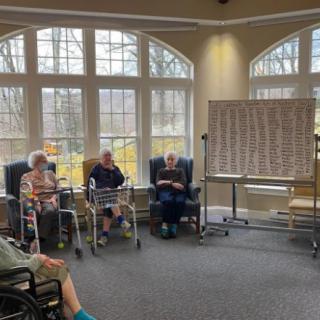 A group of elderly people sitting in wheelchairs play a game of bingo inside a well-lit room.