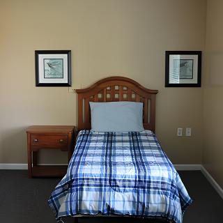 A neatly arranged bedroom with a single bed and wooden headboard, flanked by a nightstand.
