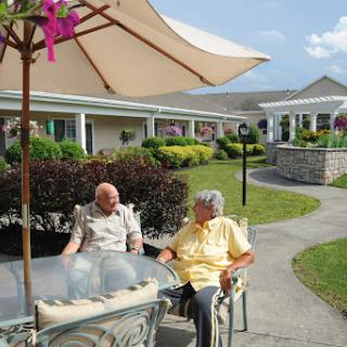 Two seniors enjoying a conversation under an umbrella in a serene outdoor setting.