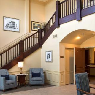 A cozy lobby interior featuring a wooden staircase, comfortable seating area, and wall decor.