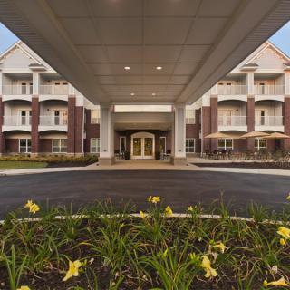 The entrance of a modern building with landscaped flowers along the pathway.