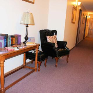 A cozy hallway with a black armchair and a wooden table featuring books and a lamp.