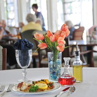 A beautifully set restaurant table with a meal, flowers, and condiments.