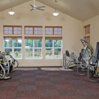 A well-lit gym with exercise equipment and large windows letting in daylight.
