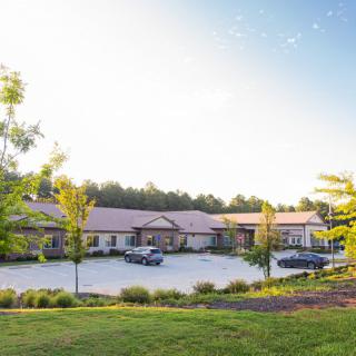 A modern building with a parking lot and surrounded by trees on a clear day.