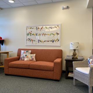 A cozy living room area featuring a sofa, artwork on the wall, and a side table with a lamp.