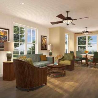A well-lit living room with modern furniture, including a sofa set, tables, and decorative lamps under a ceiling fan.