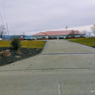A view of a building from a long driveway, surrounded by green grass under a cloudy sky.