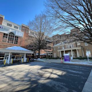 A view of a multi-story building with a canopy entrance and bare trees in the foreground under a clear blue sky.