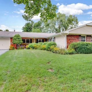 A suburban house with a well-maintained lawn and surrounding trees under a clear sky.
