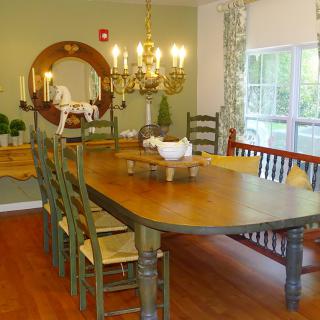 A cozy dining room with a large wooden table, surrounded by chairs, accented with a decorative chandelier and mirror.