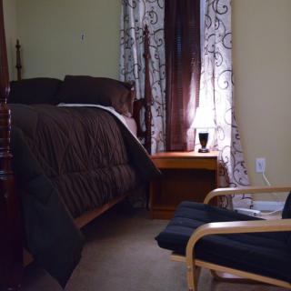 A cozy bedroom with a neatly made bed, an armchair, and a lamp on the nightstand.