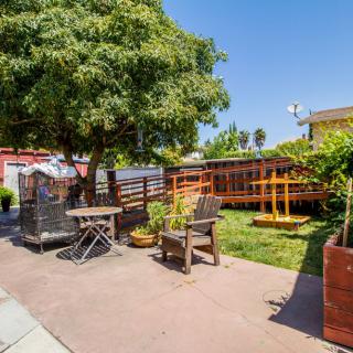 A sunny backyard with a patio featuring outdoor seating, a large tree, and a wooden deck.