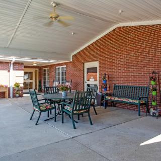 A covered patio area with outdoor seating, featuring tables and chairs against a brick wall.