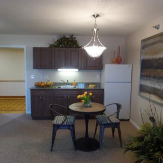 A cozy kitchen and dining area with a small table and chairs, featuring a fridge and stylish light fixture.