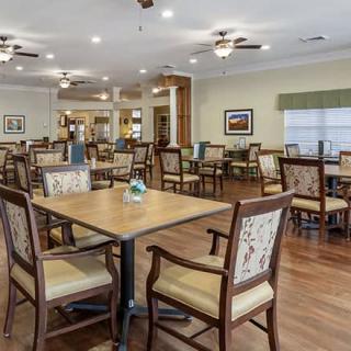 A spacious dining area with multiple tables and chairs, featuring ceiling fans and wood flooring.