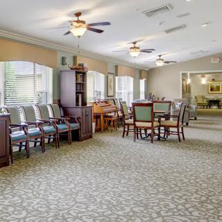 A spacious dining room with multiple tables, chairs, large windows, and ceiling fans.