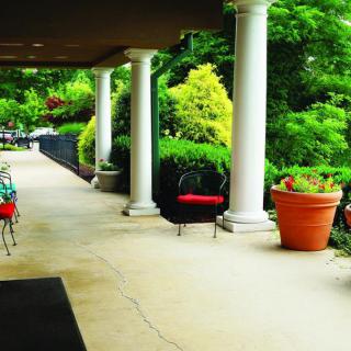 A serene patio with columns and chairs, surrounded by lush greenery and potted plants.