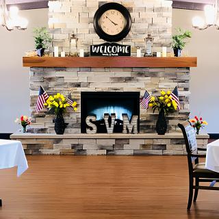 A cozy interior with a decorated fireplace, adorned with a welcome sign and surrounded by flowers and flags.