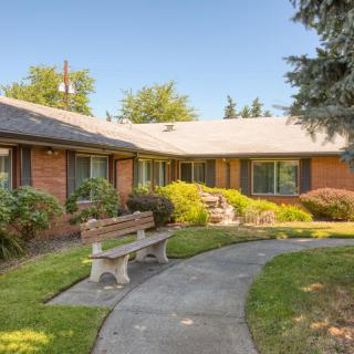 A brick house with a pathway and bench surrounded by trees and bushes.