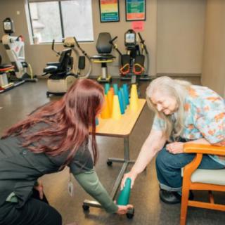 A physical therapist assists an elderly woman during a rehabilitation exercise with cones.