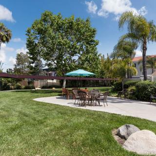 A peaceful residential backyard with a patio set under an umbrella, surrounded by lush lawn and trees.
