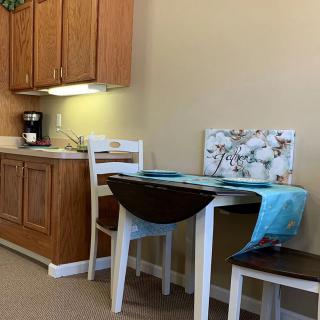 A cozy kitchen nook with a wooden table and chairs, next to a set of cabinets and coffee maker.