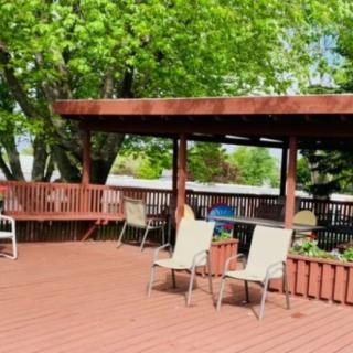 Spacious outdoor patio deck with chairs and a pergola, surrounded by lush green trees.